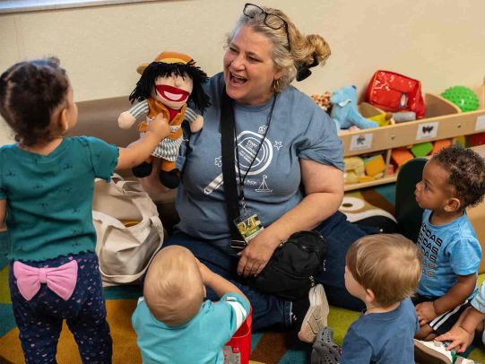 Teacher uses a hand puppet to engage a group of toddlers during an interactive classroom activity.