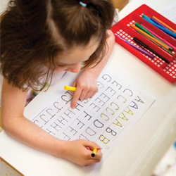 Niño practicando el trazado de letras en una hoja de trabajo del alfabeto