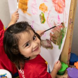 Young child smiling while painting at classroom art easel