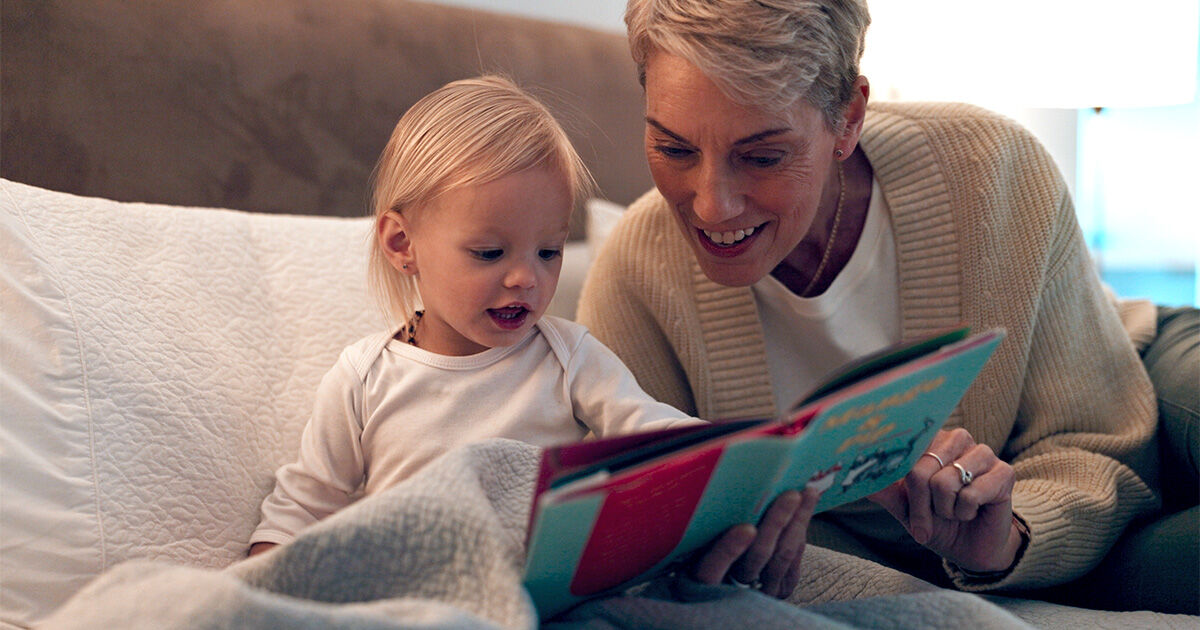 A parent and young child sharing a bedtime story while sitting together on a bed.