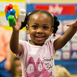 Preschool-age child smiling and holding up colorful counting toys during classroom activity