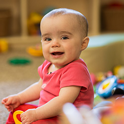 Infant sitting on classroom floor and holding toy
