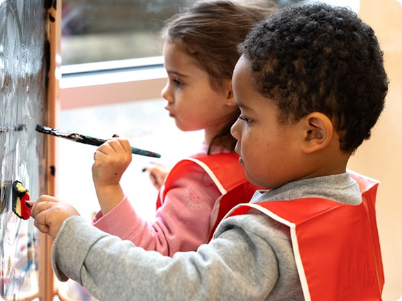 Two children painting at a classroom easel