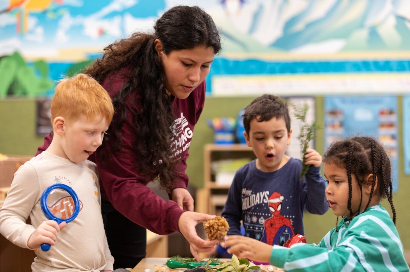 Teacher guiding three children as they explore natural materials during a classroom activity.